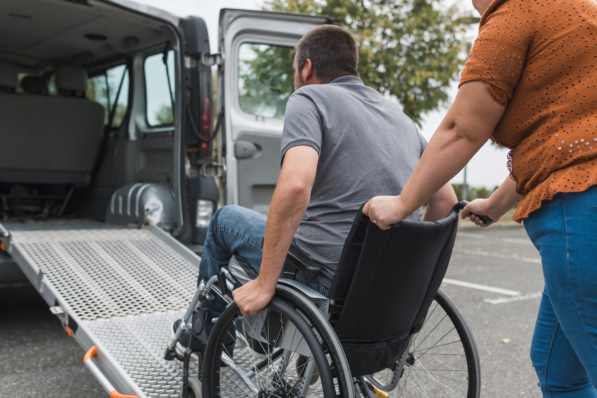 Assistant for people with disability pushing a wheelchair user up the car ramp